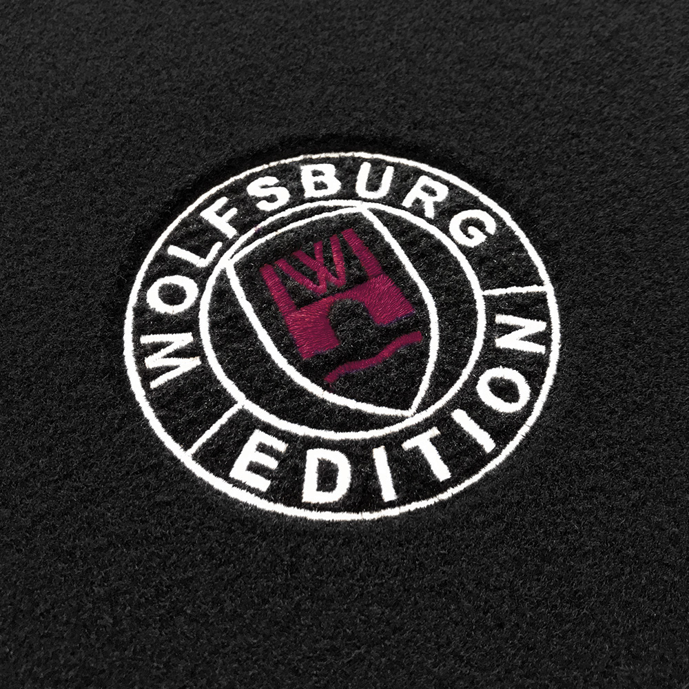 Das gestickte Wolfsburg Editions Logo auf einem schwarzen Teppich und das Logo ist in bordeaux.