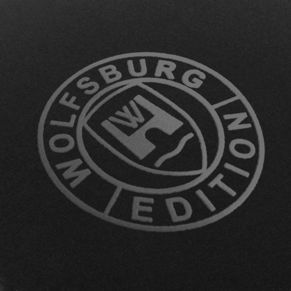 Das Wolfsburg Editions Logo auf einem schwarzen Teppich und das Logo ist in dunkelgrau.