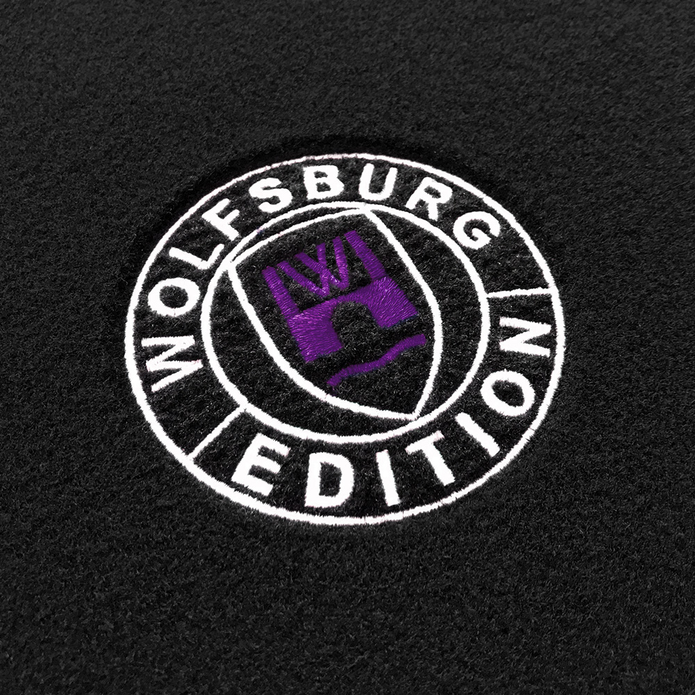 Das gestickte Wolfsburg Editions Logo auf einem schwarzen Teppich und das Logo ist in lila.